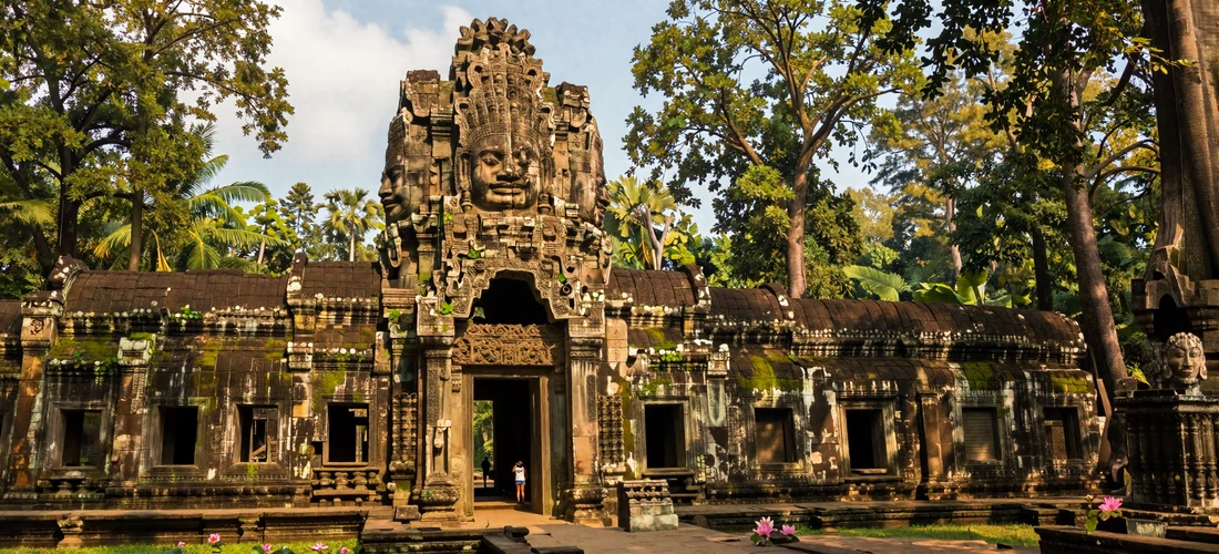 Ancient Angkor Thom gate with stone faces surrounded by tropical jungle and lotus pond in warm golden light