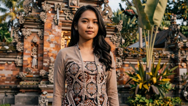 Beautiful Indonesian woman in batik kebaya near a Javanese temple with tropical vegetation at golden hour