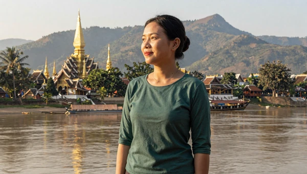 Laotian woman near the Mekong River in Luang Prabang with golden temple spires and lush mountains
