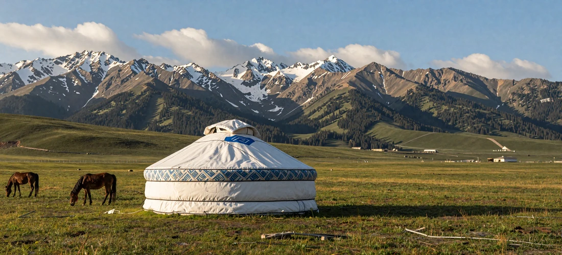 Traditional Kyrgyz white yurt on a green alpine jailoo meadow with horses grazing and dramatic Tian Shan mountain peaks under golden afternoon light